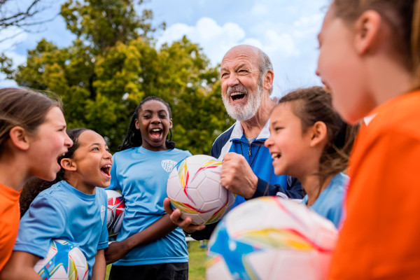 A senior man coaching a youth girls soccer team